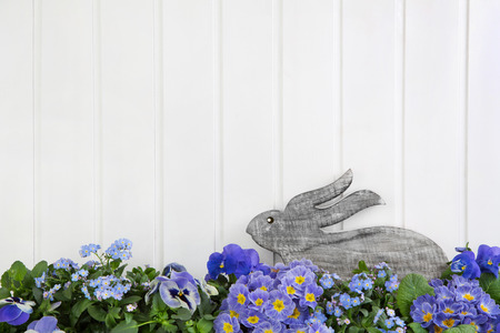 Easter bunny sitting in blue and purple spring flowers. Idea for a greeting card background in country style.の写真素材