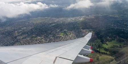 Airplane window view showing wing of plane flying over clouds and over a town