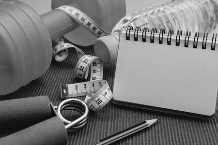 Lay Flat - Dumbbell, Measuring Tape, Hand Grip, Mineral Water, Fresh Apple, Pencil & Blank Notebook for Motivational Quotes/Words on red background - Fitness Conceptの写真素材