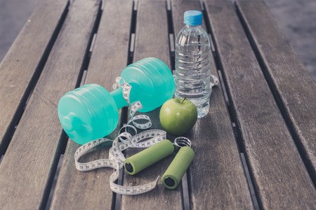 Fitness Concept - Dumbbell, Measuring Tape, Mineral Water, Fresh Apple, Hand Grip on a wooden table...