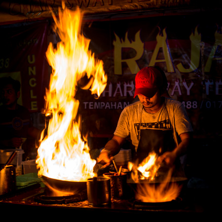 Malaysia Circa 2017 - A Chef cooking  Char Kuey Teow, a spicy rice noodle dish with prawns in his cast iron wok at his roadside stall. Big fire from his wok attracting buyers. Motion blur to show movementのeditorial素材