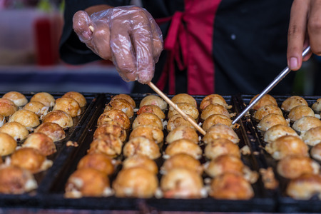 Close up hand turning takoyaki.  Takoyaki is a ball-shaped Japanese snack made of a wheat flour-based batter and cooked in a special moulded pan. Shallow depth of fieldの写真素材