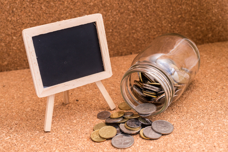 Finance Concept - A jar of coins and a blank blackboard for text. Wood Background. Shallow depth of field.の写真素材