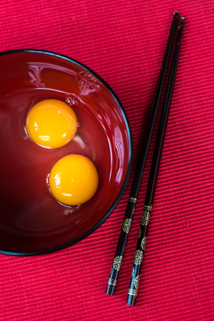 Egg Yolk in a Red Rice Bowl with chopstick, on red background, shallow depth of fieldの写真素材