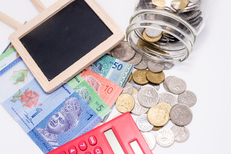Jar of Malaysia Coins, Ringgit banknotes, red calculator and blank blackboard for text. White...