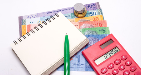 Stack of Malaysia Coins, Ringgit banknotes, red calculator and blank notepad for text. White background. Financial Concept.Shallow Depth of fieldの写真素材