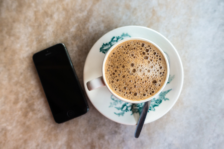 Frothy Chinese Chai/Coffee with milk in vintage cup and saucer. Smartphone next to it.