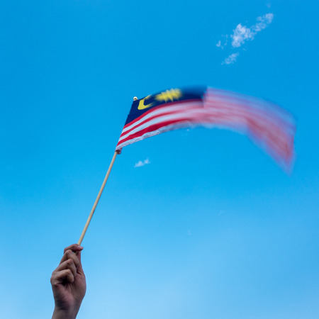 Hand Holding Malaysia Flag. Wind blowing, motion blur on flag. Blue Skyの写真素材