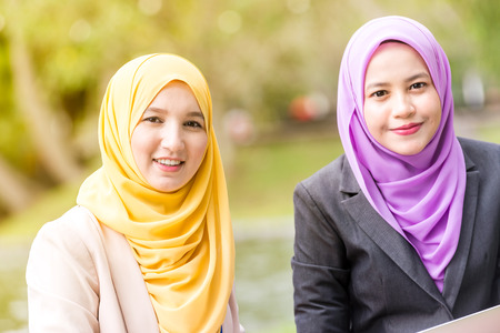 Muslim Women Entrepreneurs having a business meeting by a lake with a laptop. Looking at the cameraの写真素材