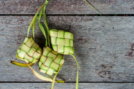 Ketupat Pouches on a wooden background. Ketupat is a type of dumpling made from rice packed inside a diamond-shaped container of woven palm leaf pouch.の写真素材