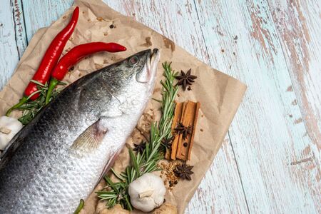 Fresh Raw Sea Bass on wooden table surrounded by fresh ingredients and spices.の写真素材