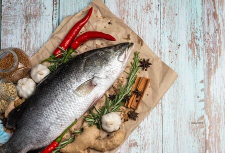 Fresh Raw Sea Bass on wooden table surrounded by fresh ingredients and spices.の写真素材