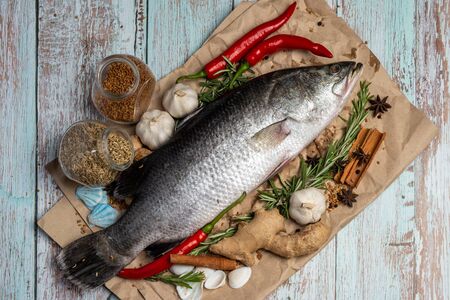 Fresh Raw Sea Bass on wooden table surrounded by fresh ingredients and spices.の写真素材