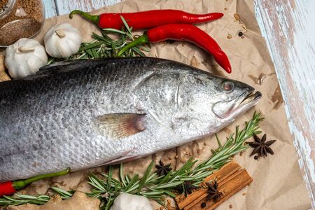 Fresh Raw Sea Bass on wooden table surrounded by fresh ingredients and spices.の写真素材