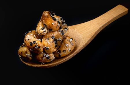 Sesame Coated Cashew Nuts on wooden spoon. Isolated on black backgroundの写真素材
