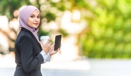Beautiful Muslim Business woman on her coffee break. Holding a smartphone, Copy space.の写真素材