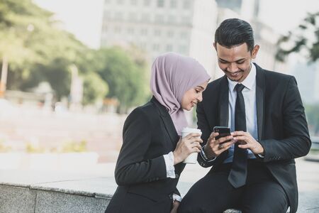 Muslim Businessman and businesswoman partner discussing using smartphone connection for work. Outdoor Setting.の写真素材