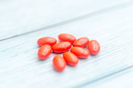 Red Colored Vitamins Pills on Wooden Background. Soft focused. Shallow depth of field