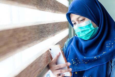 Muslim Female wearing surgical mask looking at her smartphone.  Covid-19 Coronavirus concept