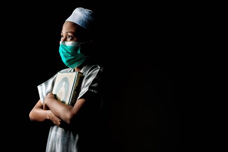 Muslim Boy wearing a surgical mask holding a Quran. Covid-19 coronavirus concept. Copy space for text.の写真素材