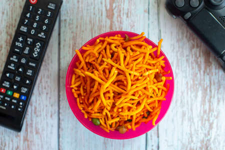 Bowl of Muruku Snack with TV remote and game pad. Shallow depth of field.