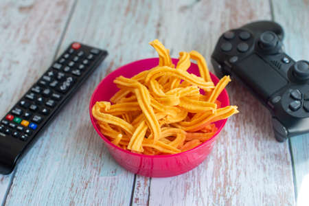 Bowl of Muruku Snack with TV remote and game pad. Shallow depth of field.の写真素材