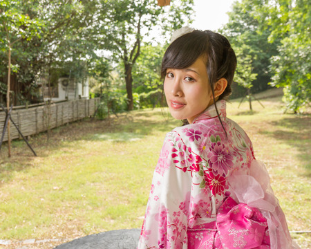Asian woman in a kimono in a Japanese style garden looking back at cameraの写真素材