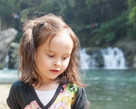 Child standing near a lake with waterfall in backgroundの写真素材
