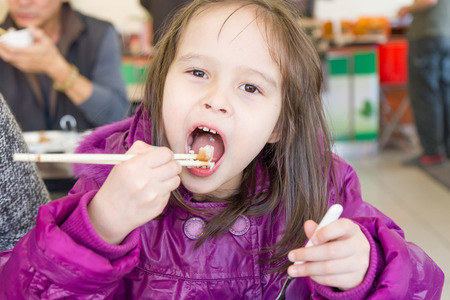 Young child eating food with Chinese chopsticksの写真素材