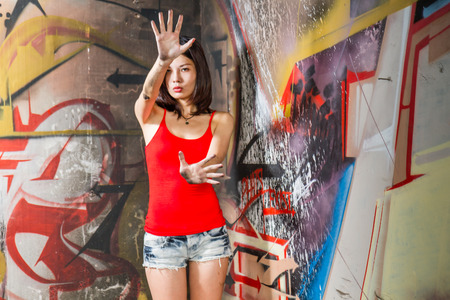 Beautiful Chinese woman with hands raised by walls filled with graffitiの写真素材