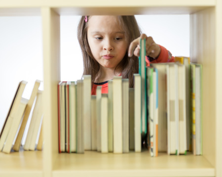 Young girl taking book from bookshelf, behind shelf. Horizontalの写真素材
