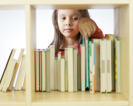 Young girl looking through books in library behind shelf. Horizontalの写真素材