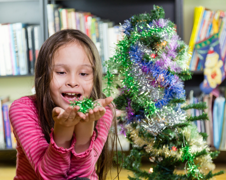 Young girl happily decorating Christmas tree, looking at tinsel in handsの写真素材