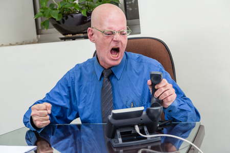 Angry businessman at desk on phoneの写真素材