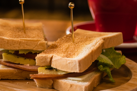 Coffee in red cup and saucer with toasted ham and cheese sandwichの写真素材