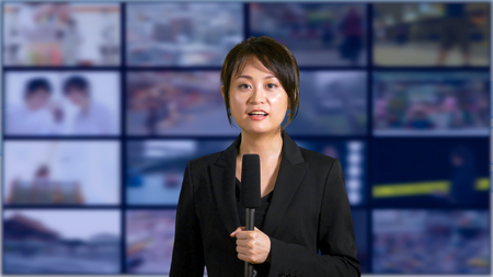 Asian American female news anchor in studio with screens in backgroundの写真素材