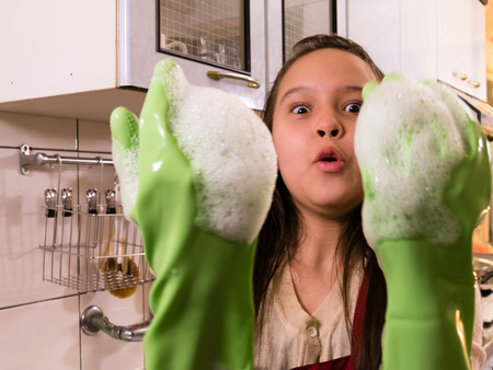 Tween Asian American girl washing dishes, showing foamy gloves with funny expressionの写真素材