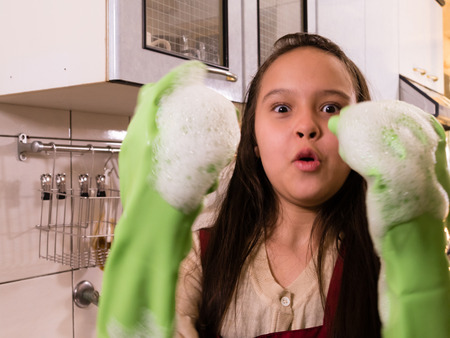 Tween Asian American girl washing dishes, showing foamy gloves with funny expressionの写真素材