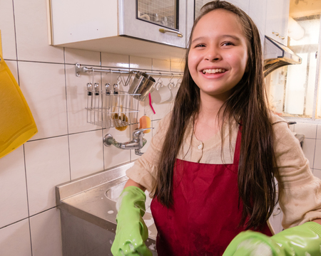Tween Asian American girl washing dishes, showing foamy gloves with funny expressionの写真素材