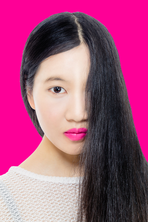 Teenage Asian American girl with hair covering half face on pink backgroundの写真素材