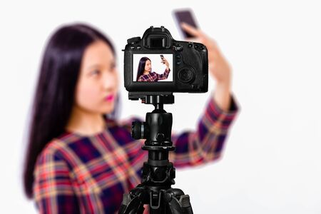 Focus on live view on camera on tripod, teenage girl  taking selfie image on back screen with...