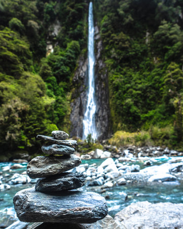 A waterfall sits in the back with a rock stack in frontの写真素材