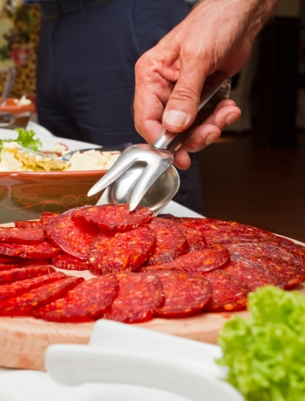 Human hand holding tongs over plate of sliced salamiの写真素材