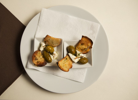 Restaurant shot of tiny bruschetti mezze style feta cheese and green olives. Finger food concept See...