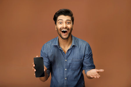A young man in a blue shirt is showing his smartphone screen towards the camera with a big smile.の写真素材