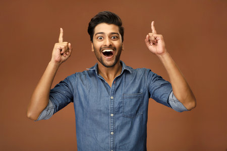 A guy pointing two fingers up at copy space while looking at the camera.