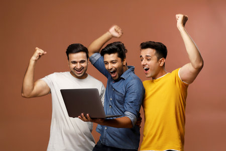 Three casual men are celebrating while looking at the laptop screen, with hands up and fists clenched.の写真素材