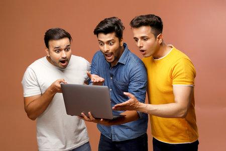 Three surprised men in casual outfits are looking at a laptop with amazement while standing.の写真素材