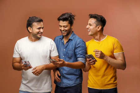 Three guys are laughing and holding their smartphones in their hands while posing.の写真素材