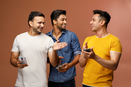 Three cool buddies are enjoying watching videos on mobile while standing in front of the camera.の写真素材